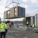 Crew setting a modular building section while the connection area is prepared